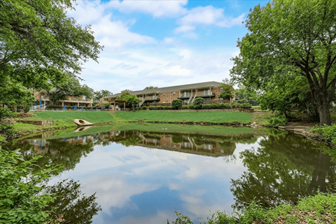 A serene landscape with a pond, trees, and a building in the background.