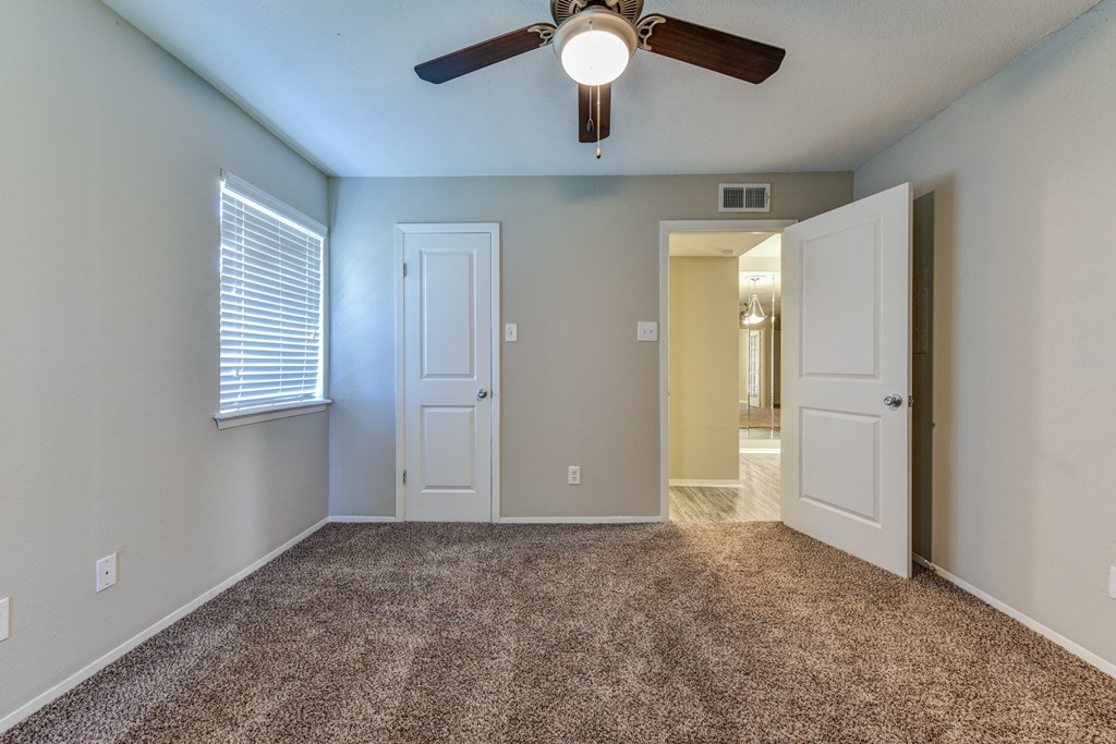 an empty living room with a ceiling fan and a door to a hallway