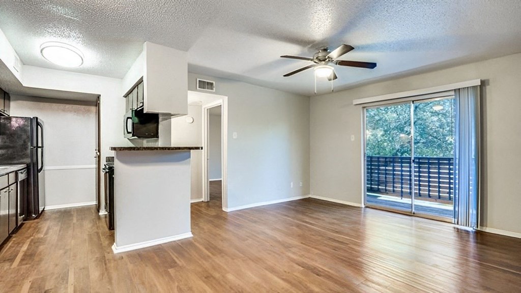 an empty living room with a kitchen and a ceiling fan  at Creek on Calloway, Richland Hills, TX