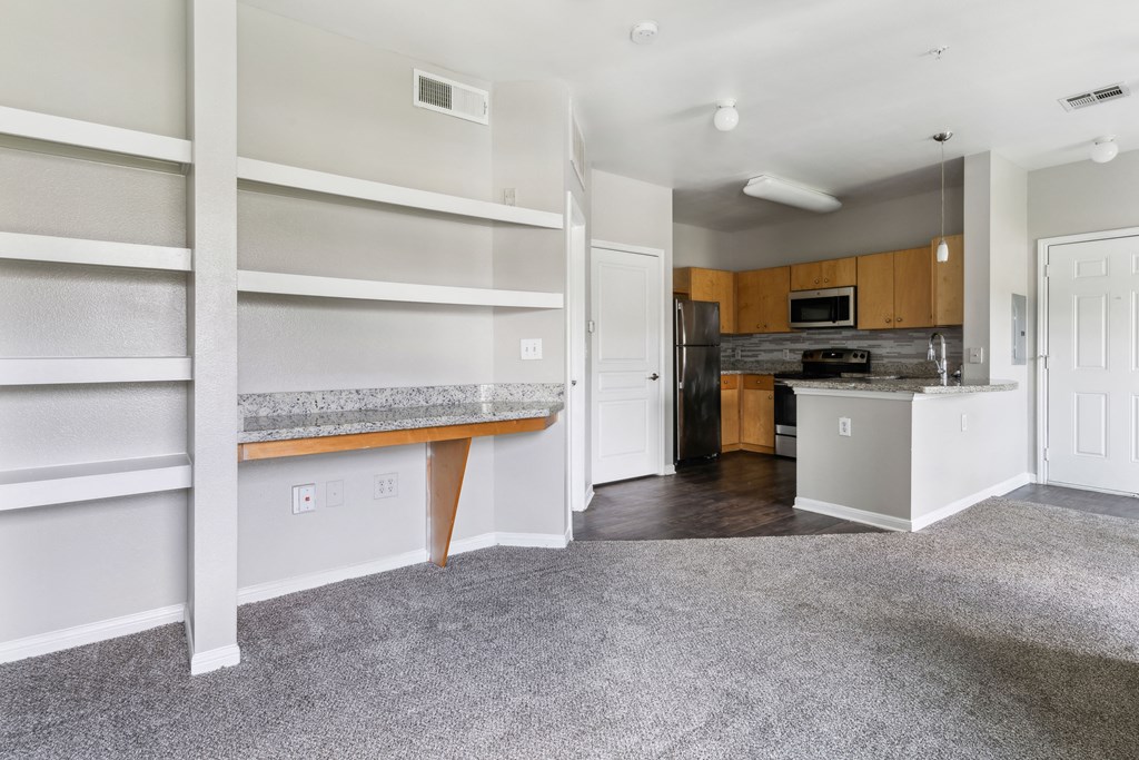 an empty living room with white shelves and a kitchen