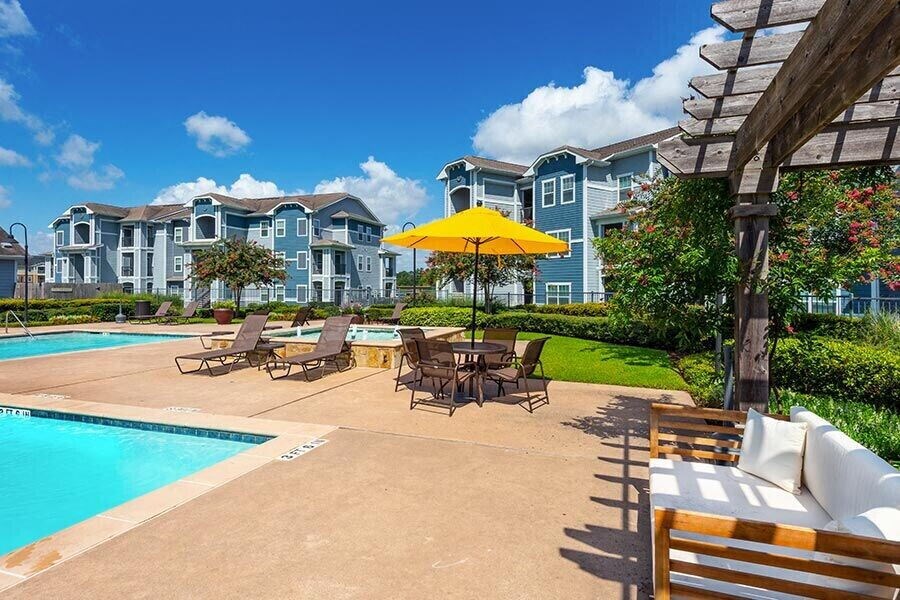 a pool with chairs and umbrellas in front of an apartment building