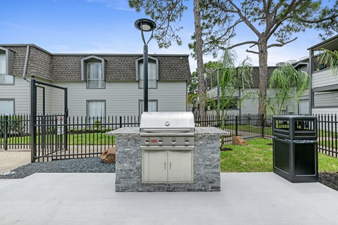 an outdoor kitchen with a grill and a trash can in front of a house
