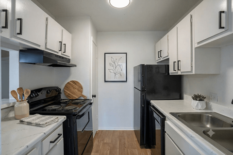 A black refrigerator sits in a kitchen with white cabinets.