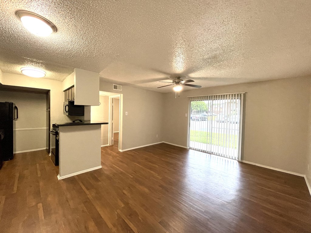 an empty living room with a kitchen and a ceiling fan