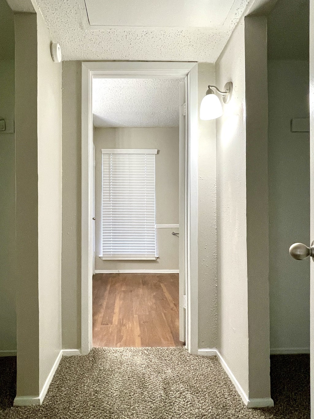 an empty hallway with a door to a bedroom and a window with a white blind