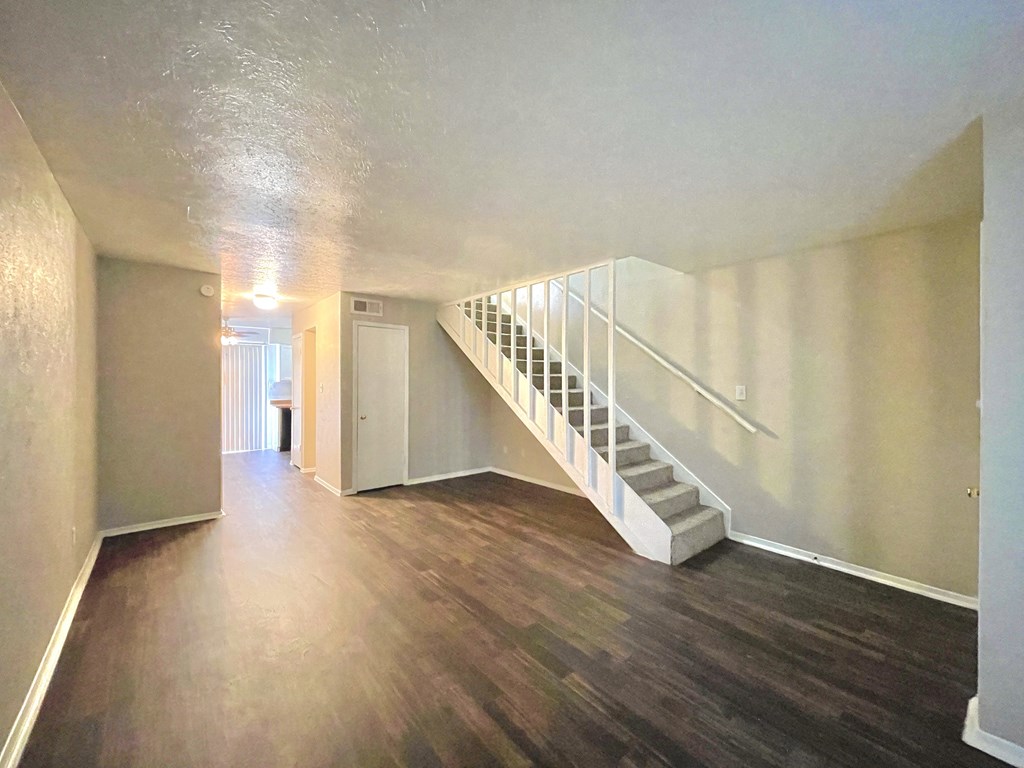 an empty living room with a staircase and wood floors