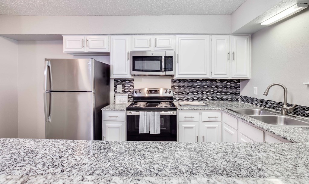 A kitchen with a refrigerator, microwave, oven, and sink.