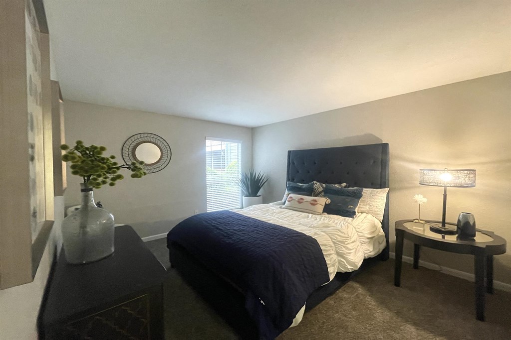 a bedroom with a bed and a nightstand with a lamp and a window