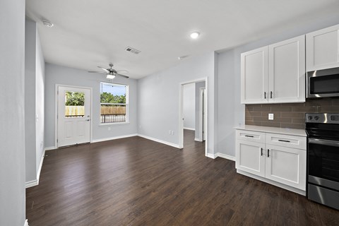 an empty kitchen and living room with white cabinets and a ceiling fan