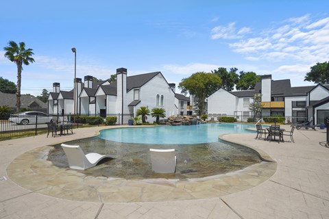 A pool surrounded by a stone patio and chairs.