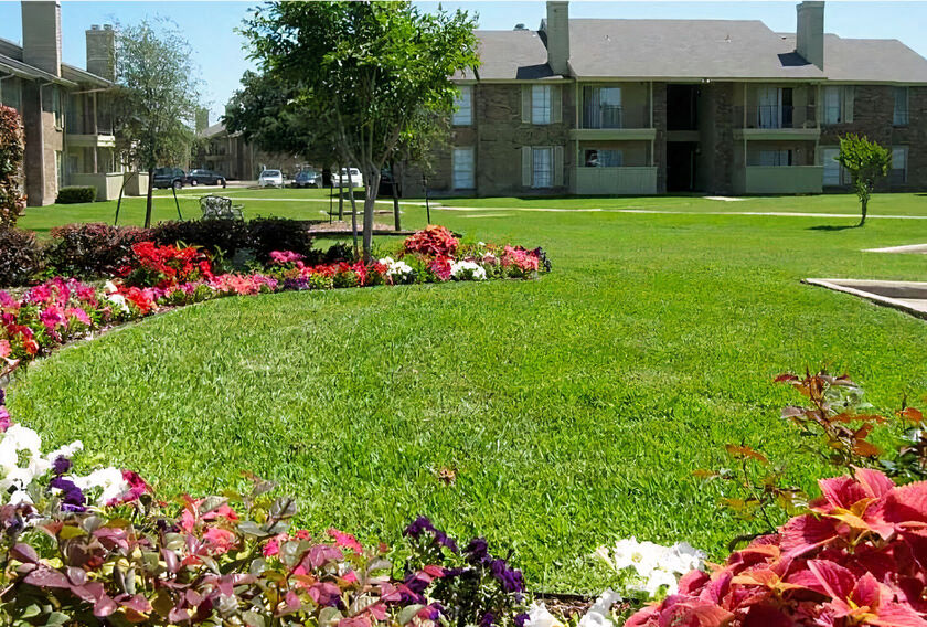 a lush green lawn with flowers in front of an apartment building  at Wymberly Pointe, Grand Prairie, TX, 75052