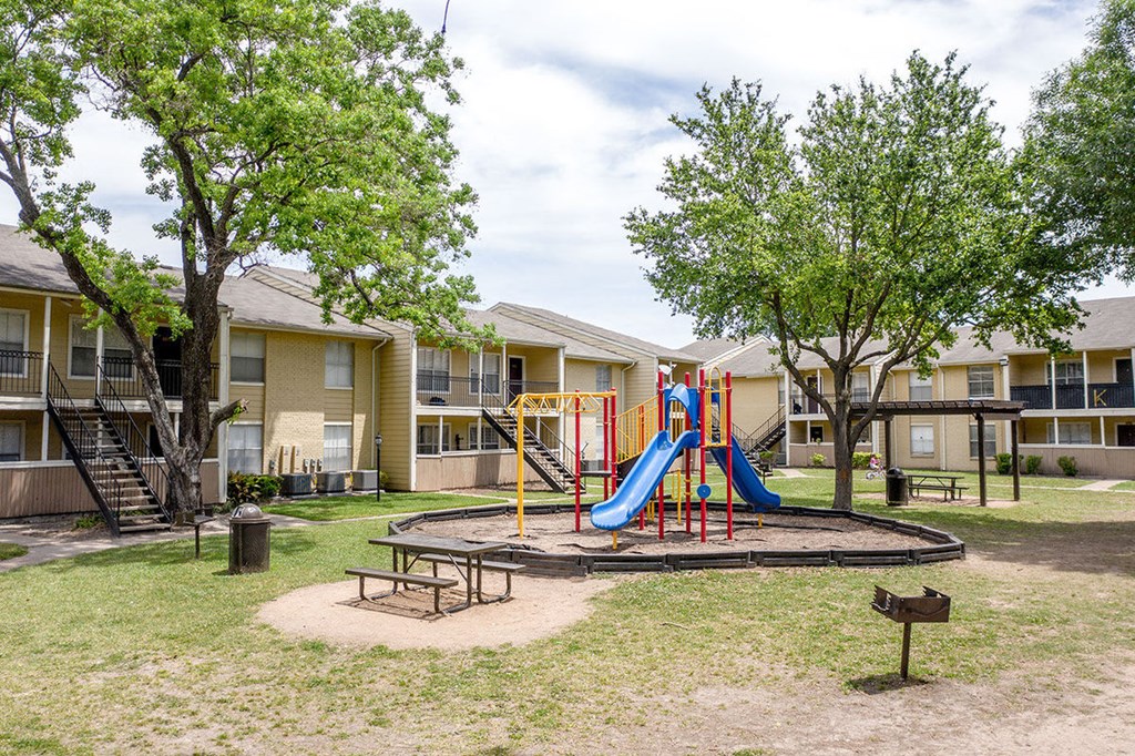 A playground with a slide and a picnic table in front of apartment buildings.