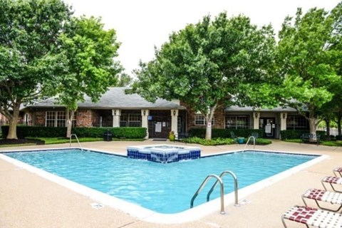 A swimming pool surrounded by trees and a building in the background.