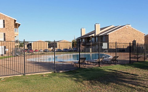 a swimming pool in front of a house behind a fence