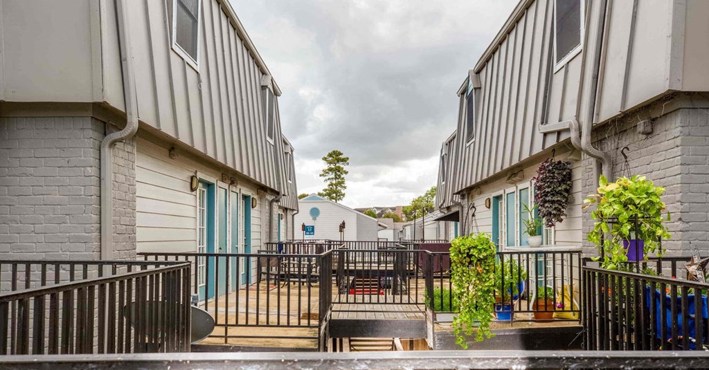 A view of a courtyard between two buildings with a metal fence and a small tree in the middle.