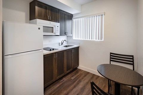 A kitchen with a white refrigerator, brown cabinets, and a black chair.