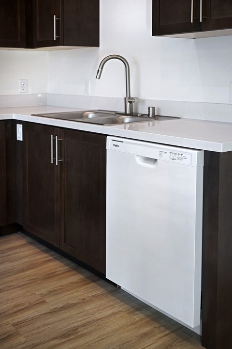 A white dishwasher is in a kitchen with dark brown cabinets.