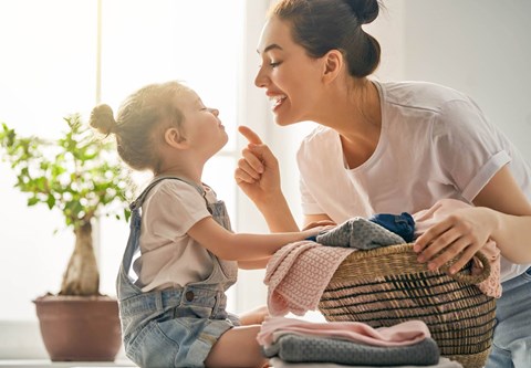 A woman and a child are sitting together, with the woman holding a basket of clothes.
