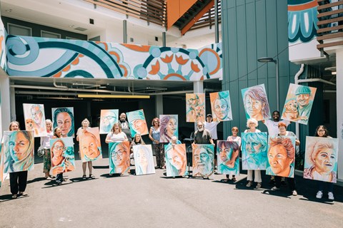 A group of people holding up paintings of women's faces.