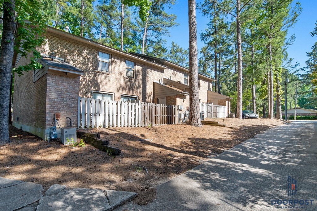 the front of a brick house with a white fence and trees
