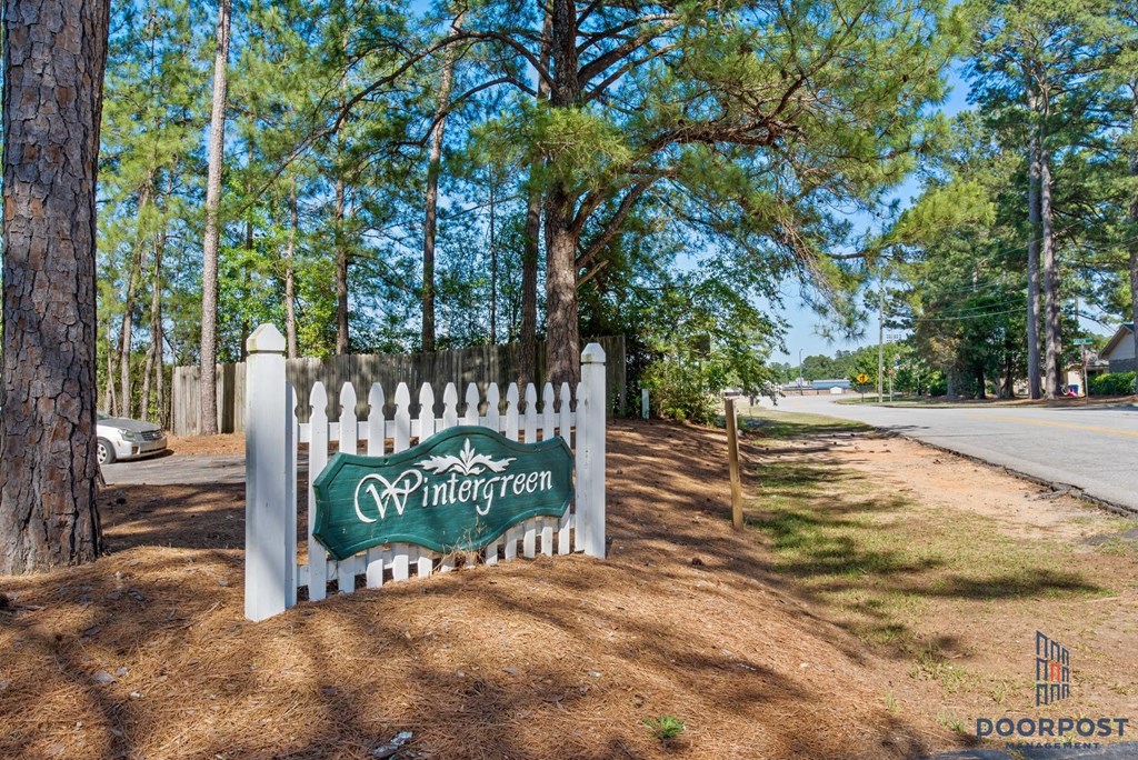 a white picket fence with a sign in front of some trees