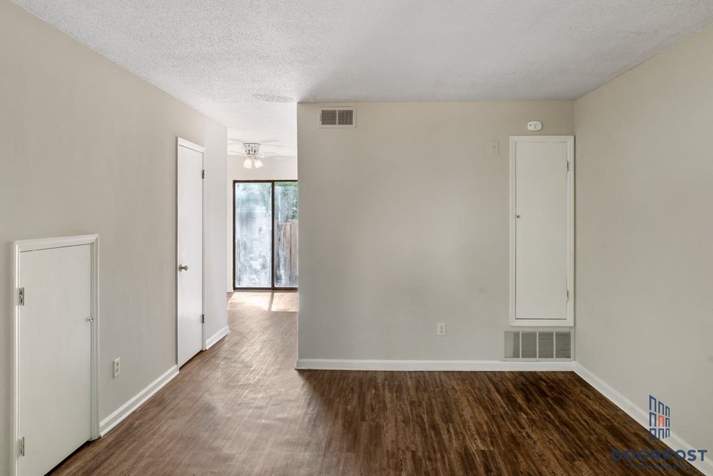 the living room and dining room of an apartment with wood flooring and white walls
