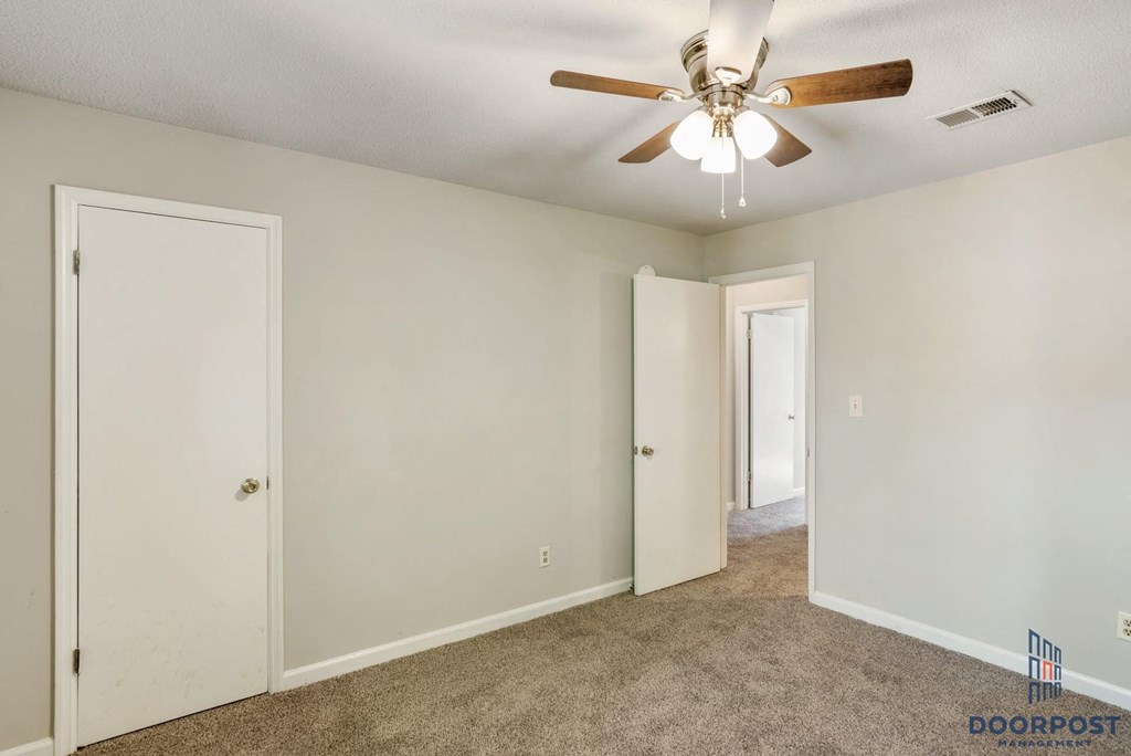 an empty living room with a ceiling fan and a door to a hallway