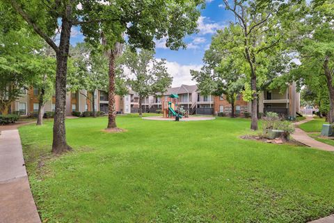 a park with green grass and trees in front of apartment buildings