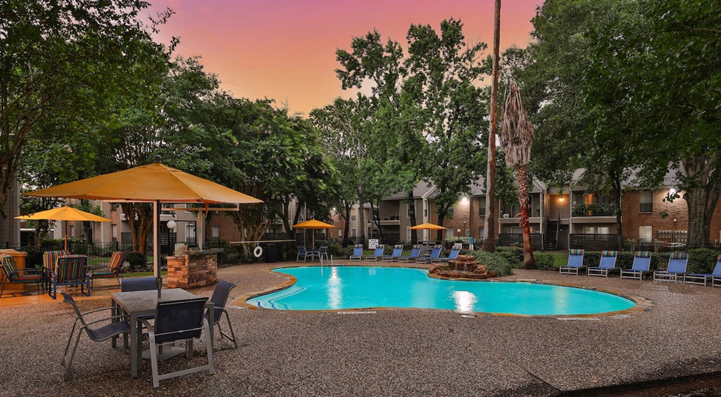 a resort style swimming pool with tables and umbrellas at dusk