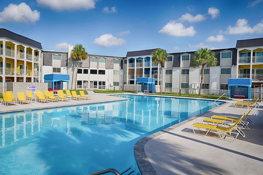 a large swimming pool with yellow chairs in front of apartment buildings