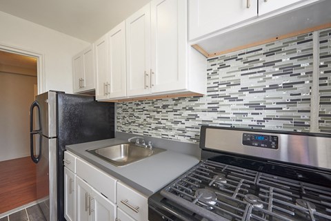 A modern kitchen with a black refrigerator, stainless steel stove, and white cabinets.