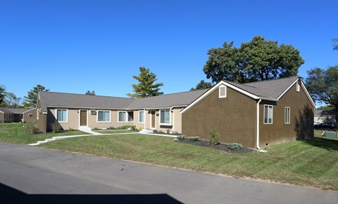 A brown house with a white door and windows is surrounded by a grassy area.