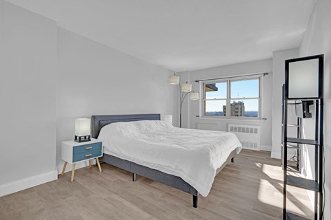 A bedroom with a bed, nightstand, and a window overlooking the city.