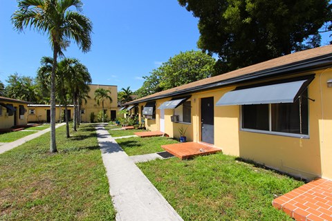 A yellow building with a black awning is surrounded by green grass and trees.