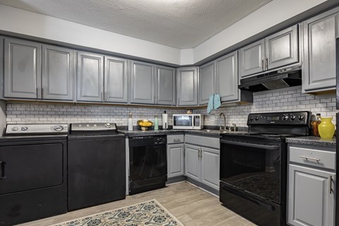 A kitchen with black appliances and grey cabinets.
