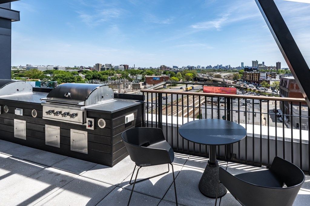 A barbecue grill is on a balcony with a table and chairs.