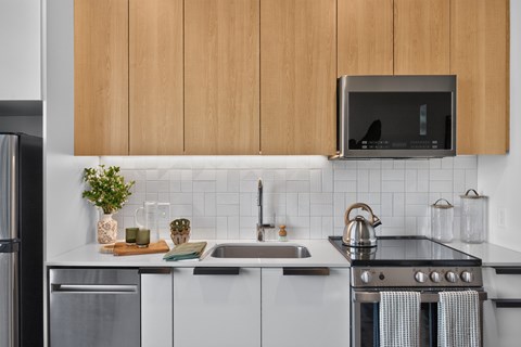 A modern kitchen with a stainless steel refrigerator, a microwave above the stove, and a sink with a kettle on it.