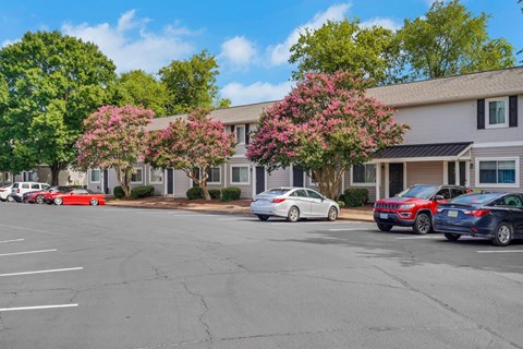 A parking lot with cars and a building with trees in front.