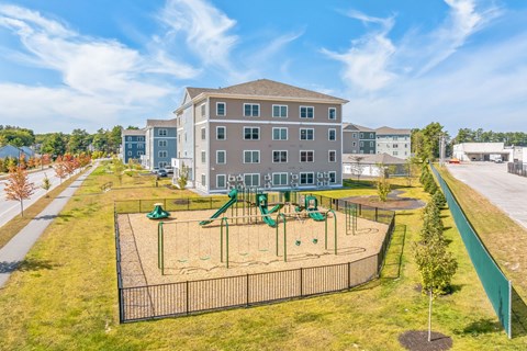 A playground with a green slide and sandbox in front of a large building.