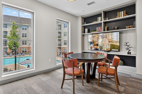 A dining room with a table and chairs and a view of a pool and buildings outside.