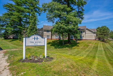 A sign for The Haven West is in the foreground of a grassy area with trees and houses in the background.