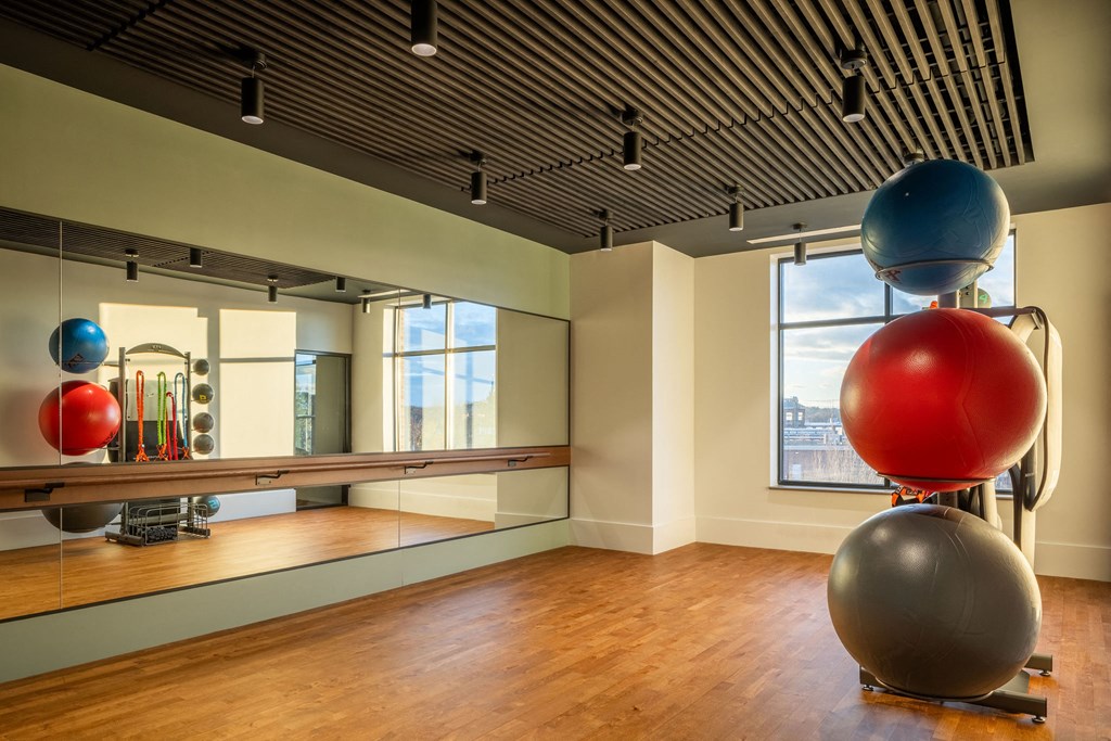 A room with a mirror, wooden floor and a blue ball on top of a red ball.