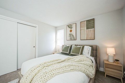 A bedroom with a bed covered in a white blanket and pillows.