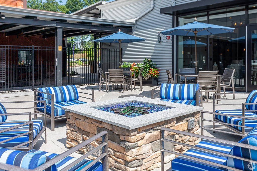 A patio with blue and white striped chairs and a stone fire pit.