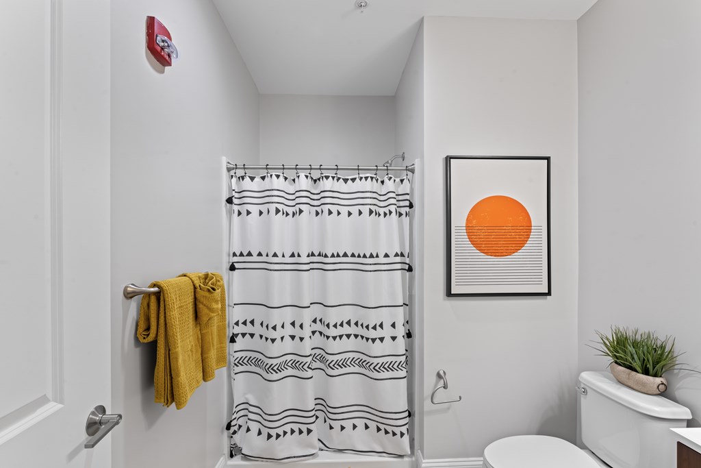 A bathroom with a yellow towel hanging on the door and a shower curtain with black and white designs.