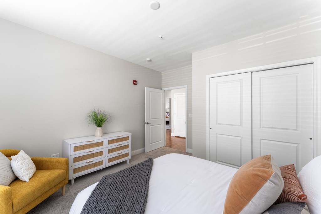 A bedroom with a bed, a yellow sofa, and a wooden dresser.