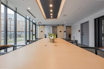 A long conference table with chairs and a vase of flowers on top.