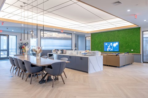 A conference room with a long table and chairs, a reception desk, and a green wall with a TV.
