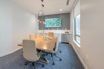 A conference room with a table, chairs, and a TV on the wall.