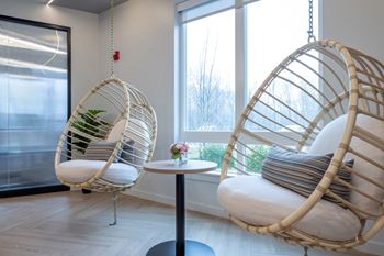 Two hanging wicker chairs with cushions and a small table with a vase of flowers.